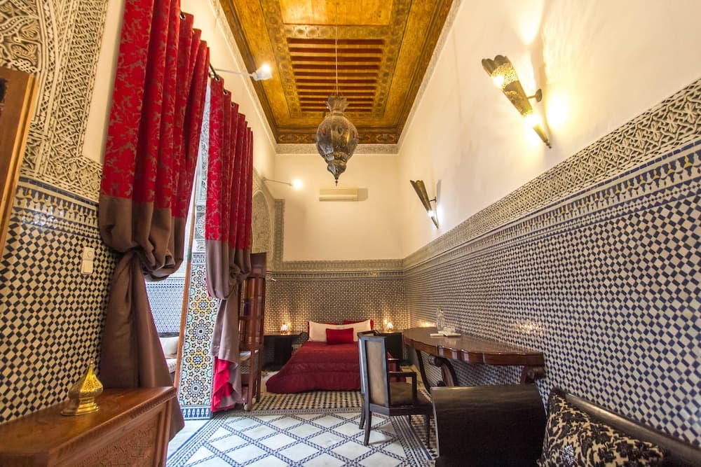 A cozy Moroccan-style bedroom with intricate tilework, warm lighting, and ornate furnishings invites travelers to experience luxurious relaxation in a traditional setting.