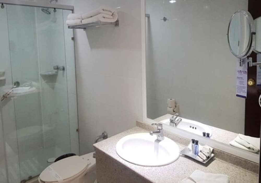 A clean and modern hotel bathroom features a glass-enclosed shower, a sleek sink with toiletries, and neatly folded towels, ideal for travelers seeking comfort and convenience.