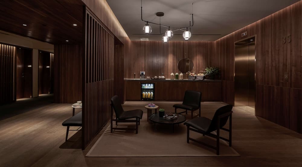 A cozy hotel lobby with warm wooden paneling, modern black leather seating, a refreshment bar, and soft lighting creates an inviting atmosphere ideal for travelers seeking relaxation and comfort.