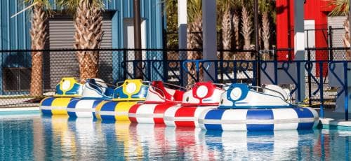 Brightly colored paddleboats float invitingly on calm pool waters beside a fenced area with palm trees, creating a playful and relaxing atmosphere ideal for family-friendly resort activities.