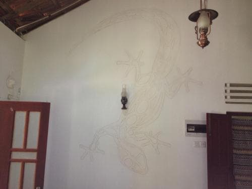 A cozy indoor space features a sketched lizard mural on a white wall, flanked by wooden doors and a vintage lamp, creating an artistic and rustic atmosphere ideal for travelers seeking unique accommodations.