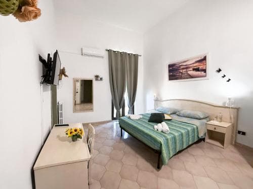 A cozy hotel room features a neatly made bed with green bedding, a desk adorned with sunflowers, and soft lighting, creating a serene atmosphere ideal for travelers seeking relaxation.