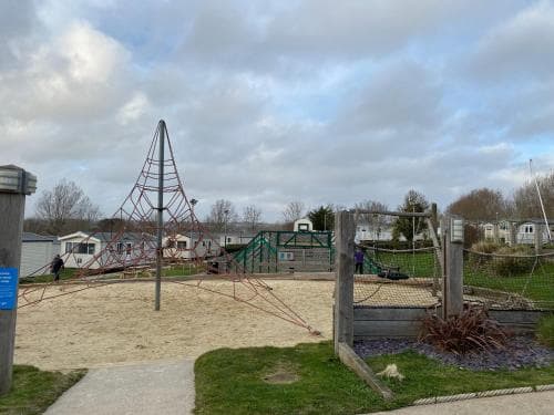A serene playground under a cloudy sky features a unique climbing structure, sandy play area, and greenery, ideal for family-friendly outdoor activities.