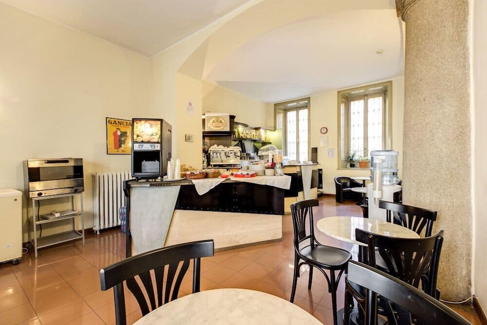 A cozy café with marble tables, black chairs, and a well-equipped bar area bathed in natural light from large windows, ideal for travelers seeking a quiet spot for breakfast or coffee breaks.