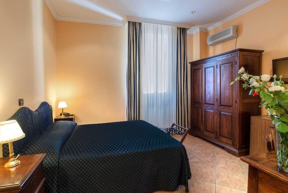 A cozy hotel room with warm beige walls, a neatly made bed with blue bedding, wooden furniture, and soft lighting creates an inviting atmosphere ideal for travelers seeking comfort and relaxation.