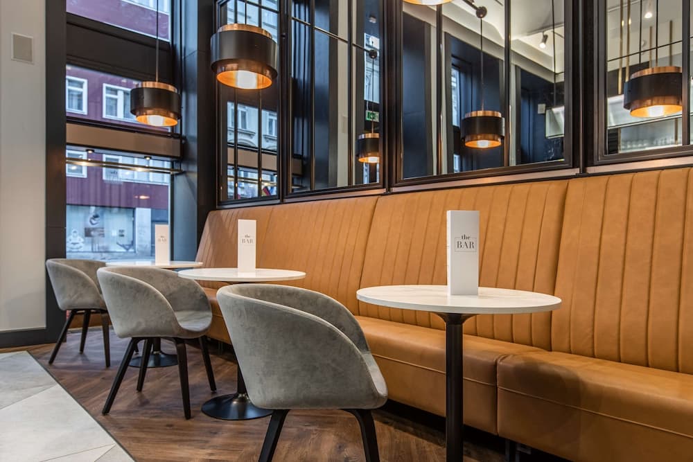 A cozy urban café features plush mustard-colored booths, modern pendant lights, and sleek gray chairs, creating an inviting atmosphere perfect for business meetings or casual dining.