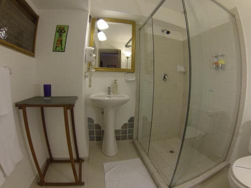 A cozy hotel bathroom features a glass-enclosed shower, white pedestal sink, wooden table, and framed mirror, creating a clean and inviting atmosphere ideal for travelers seeking comfort.