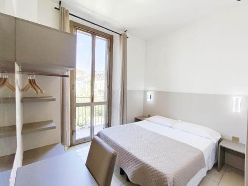 A cozy hotel room with a neatly made bed, modern furnishings, and a balcony offering natural light, ideal for travelers seeking comfort and relaxation.