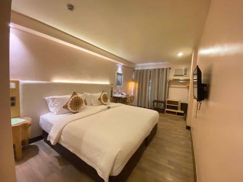 A cozy hotel room features a neatly made bed with decorative pillows, soft lighting, and a small seating area by the window, ideal for travelers seeking comfort and relaxation during their stay.