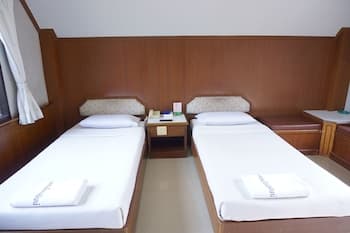 A cozy hotel room features two neatly made single beds with white linens, wooden furnishings, and a calm atmosphere, ideal for travelers seeking simplicity and comfort.