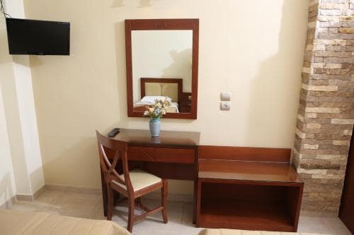 A cozy hotel room features a wooden desk with a vase of flowers, a mirror, and a stone wall, creating a warm and inviting atmosphere ideal for travelers seeking comfort and relaxation.