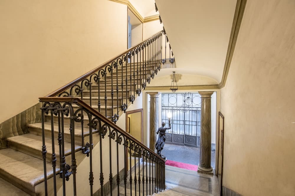 A grand staircase with ornate iron railings leads to an elegant entrance hall featuring classical columns and a statue, ideal for travelers exploring historic architecture and luxurious interiors.