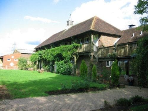 A charming countryside retreat features a rustic brick house with a thatched roof, lush greenery, and a tranquil garden, ideal for a peaceful getaway or family vacation.