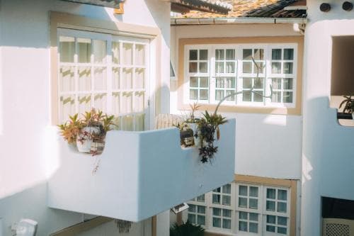 A serene courtyard with white walls, tiled roofs, and potted plants bathed in sunlight creates an inviting atmosphere ideal for a tranquil getaway or vacation rental experience.