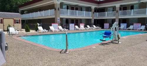 A vibrant outdoor pool area at a motel features lounge chairs, accessibility equipment, and a serene atmosphere, ideal for travelers seeking relaxation and convenience.