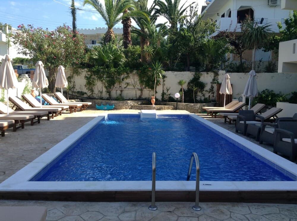 A serene resort pool area surrounded by lush palm trees and blooming flowers offers a tranquil escape, perfect for travelers seeking relaxation under sunny skies.