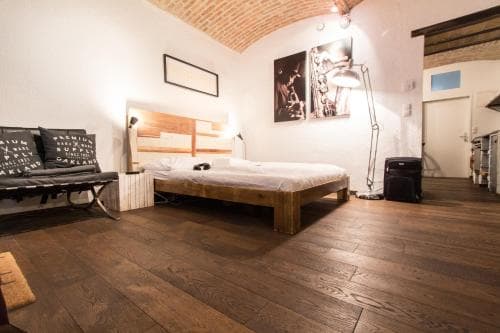 A cozy loft bedroom with exposed brick ceilings, wooden floors, and modern furnishings creates an inviting atmosphere, perfect for travelers seeking a stylish urban retreat.
