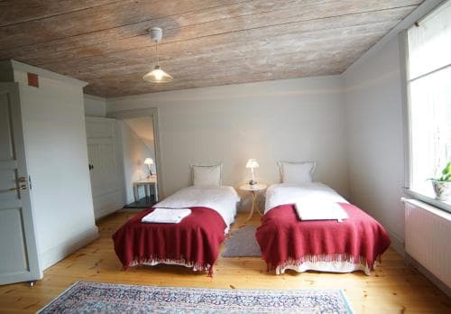 A cozy, rustic bedroom with twin beds adorned in red blankets, wooden floors, and exposed ceiling beams offers a serene retreat for travelers seeking a quaint and charming accommodation experience.