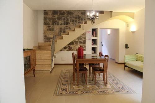 A cozy living space featuring a rustic stone staircase, wooden dining set on an ornate rug, and soft lighting, ideal for travelers seeking a charming and inviting rental accommodation.