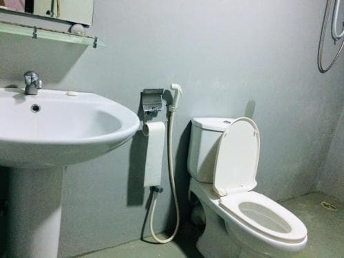A simple bathroom featuring a white sink, toilet, and bidet setup against plain walls, ideal for travelers seeking basic hygiene facilities in budget accommodations.