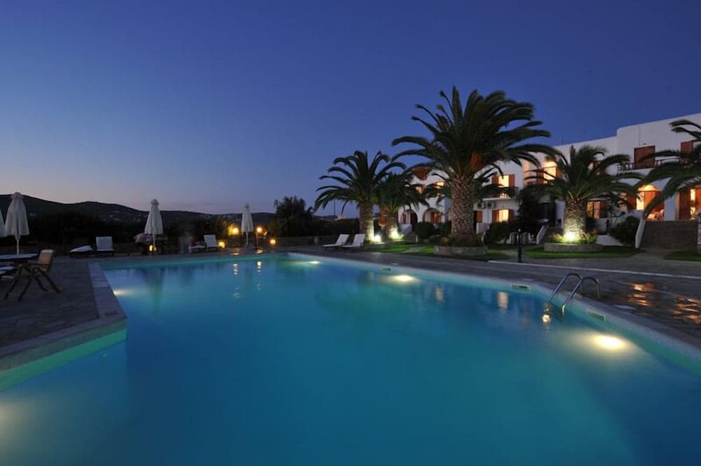 A serene evening at a luxurious resort features a glowing pool surrounded by palm trees and cozy lounge chairs, ideal for travelers seeking relaxation and tranquility.