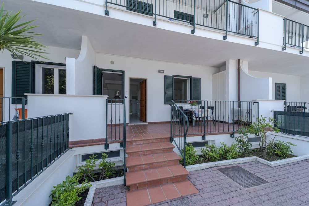 A charming Mediterranean-style apartment entrance with white walls, green shutters, and terracotta stairs invites travelers seeking a cozy and serene vacation retreat.