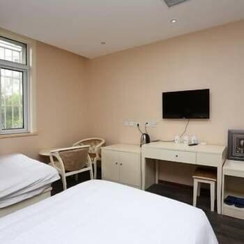 A cozy hotel room with beige walls, two neatly made beds, a desk with a TV above it, and natural light from a window creates a serene atmosphere ideal for travelers seeking comfort and simplicity.
