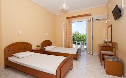 A cozy hotel room with two wooden beds, a balcony view of greenery, warm yellow walls, and simple furnishings creates a relaxing atmosphere ideal for travelers seeking comfort and tranquility.