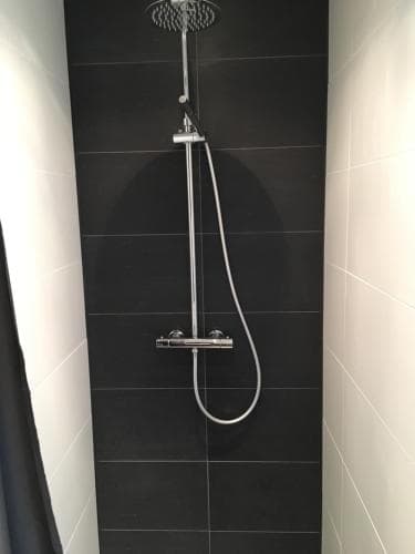 A modern bathroom shower area features sleek black tiles contrasted by white walls, equipped with a contemporary chrome showerhead and hand-held hose, ideal for travelers seeking a stylish and functional accommodation amenity.