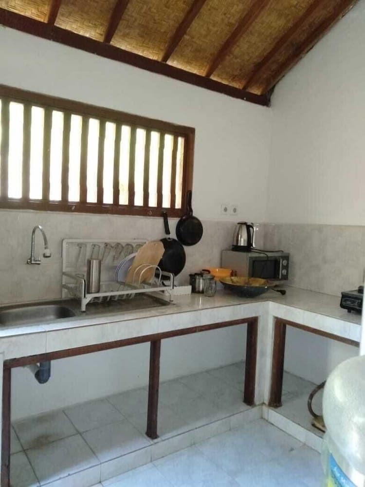 A cozy kitchen with a bamboo ceiling, tiled floor, and wooden window frames offers a rustic charm ideal for travelers seeking a homely cooking experience.