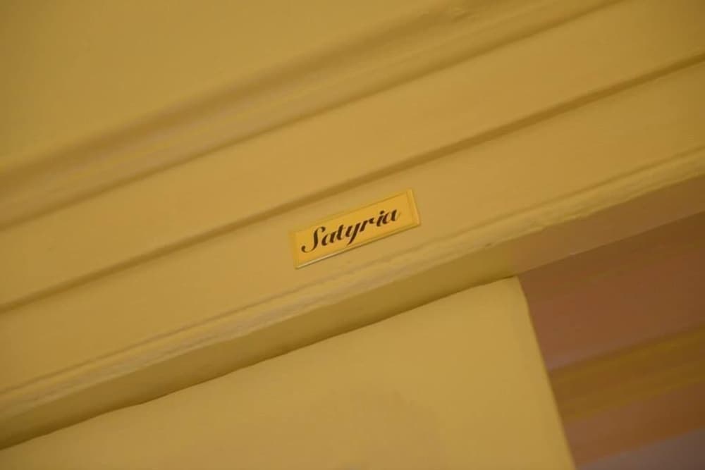 A warmly lit hotel corridor features a golden "Satyria" sign on a yellow wall, evoking a cozy and elegant atmosphere ideal for travelers seeking a refined stay.