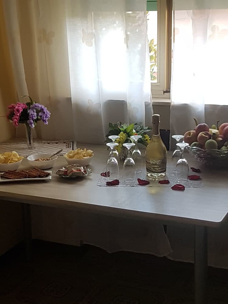 A cozy dining room bathed in soft natural light features a welcoming table set with snacks, a bottle of sparkling wine, floral arrangements, and fresh fruit, ideal for travelers seeking a warm and inviting retreat.