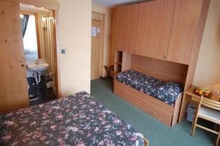A cozy hotel room with floral-patterned beds, wooden furniture, and a small dining area by the window, ideal for budget travelers seeking comfort and simplicity.