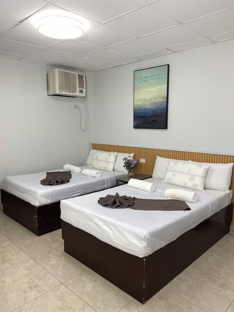 A cozy hotel room features two neatly made beds with white linens, a wall-mounted air conditioner, a serene abstract painting, and a vase of flowers, ideal for travelers seeking comfort and simplicity.