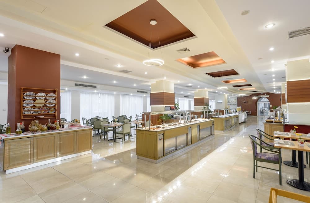 A spacious, well-lit hotel buffet area features polished floors, modern decor, and neatly arranged dining tables, creating an inviting atmosphere ideal for travelers seeking a comfortable dining experience.