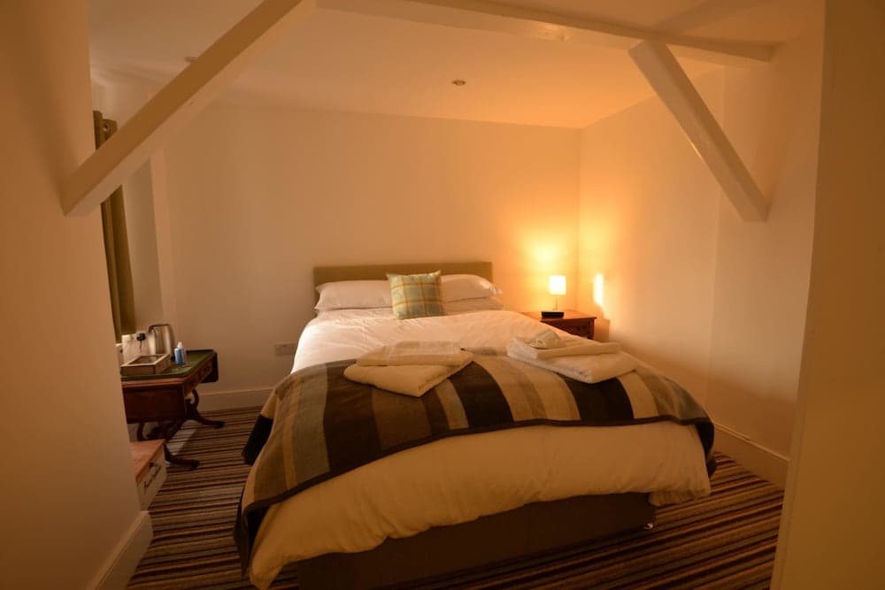 A cozy attic bedroom with warm lighting, wooden beams, neatly folded towels on the bed, and a small desk, ideal for travelers seeking a charming and intimate accommodation experience.