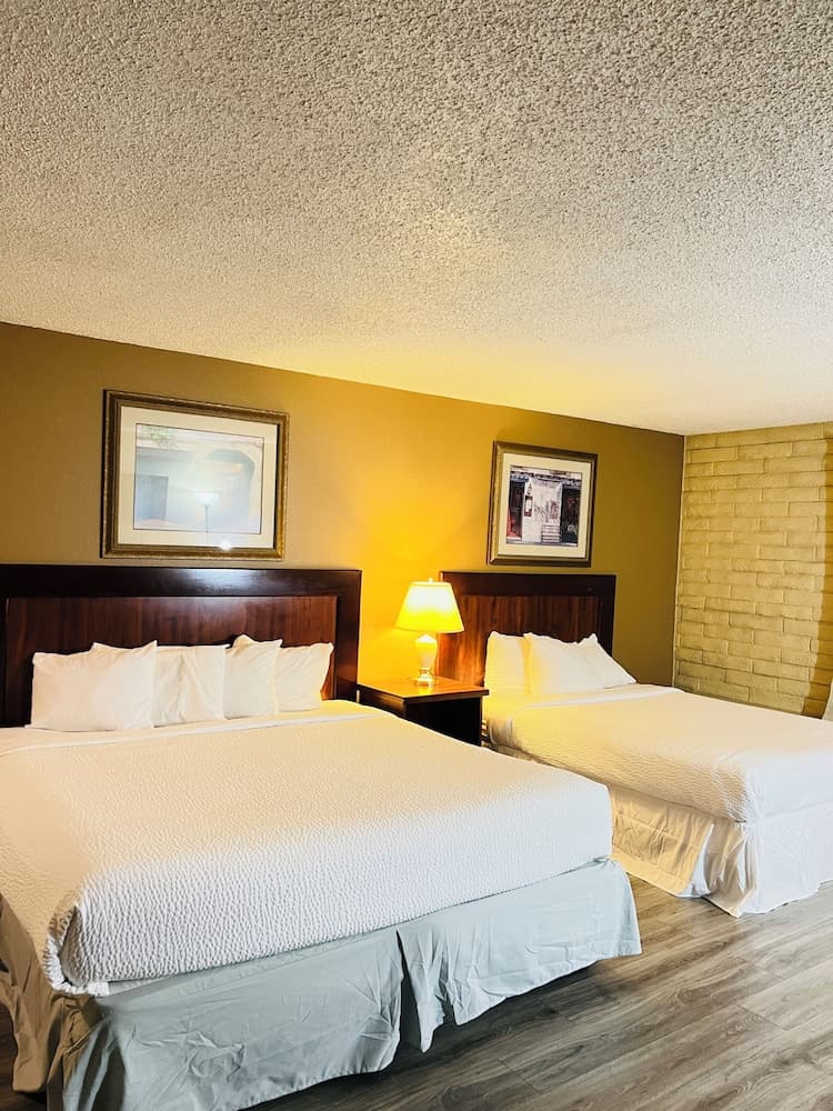 A cozy hotel room features two neatly made beds with white linens, framed artwork on mustard-colored walls, and a warm ambiance ideal for travelers seeking comfort and relaxation.