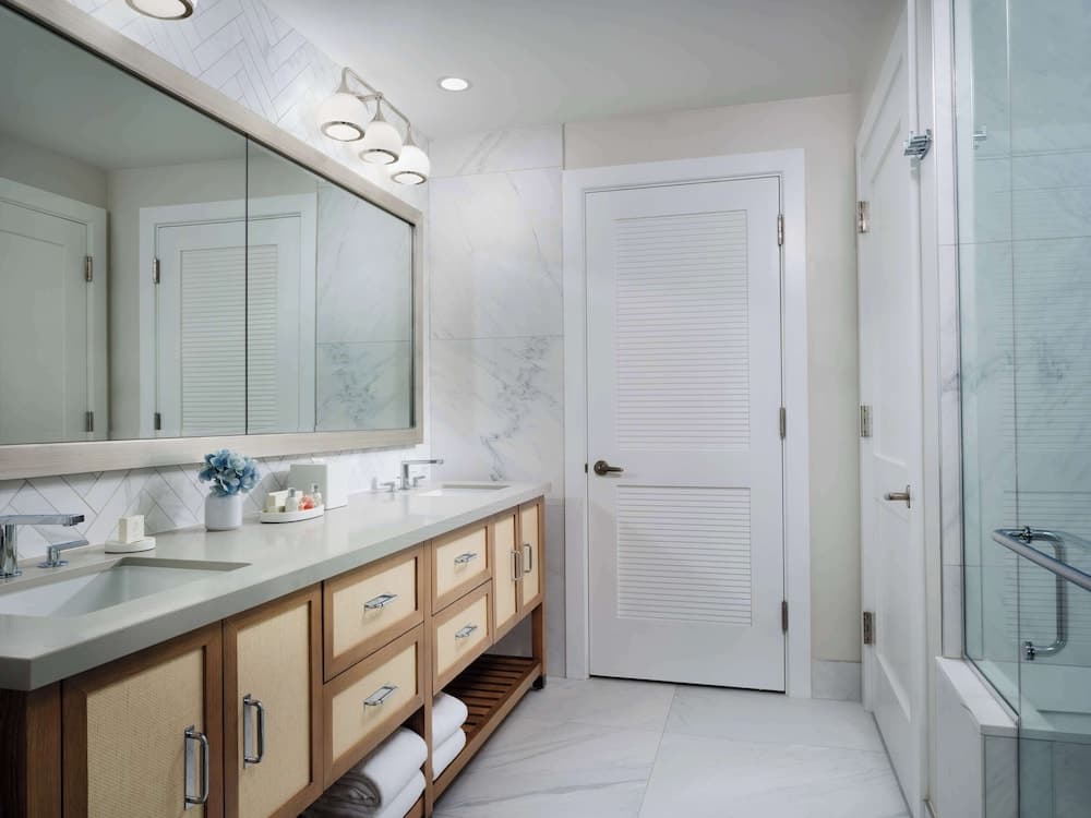 A serene luxury bathroom features a spacious vanity with dual sinks, elegant marble walls and flooring, a walk-in shower, and soft lighting, ideal for travelers seeking a relaxing retreat.