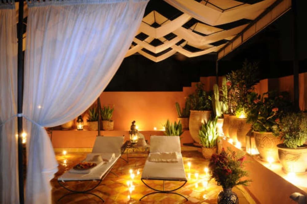 A serene rooftop terrace at night, adorned with twinkling candles, plush lounge chairs, and lush potted plants under a geometric canopy, offers an ideal spot for relaxation and romantic evenings.