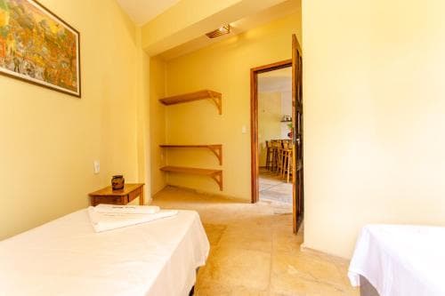 A cozy, warmly lit hotel room features a neatly made bed, wooden shelves, and an open doorway leading to a dining area, ideal for travelers seeking comfort and simplicity.