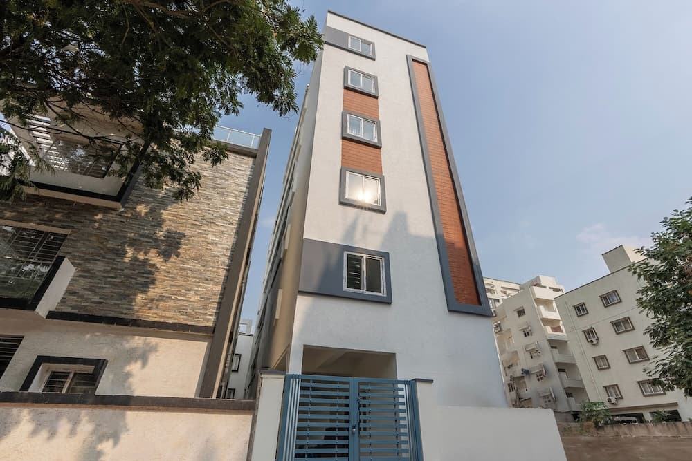 A modern residential building with a sleek white facade and orange accents stands under a clear blue sky, surrounded by lush greenery, ideal for urban living and property investment.