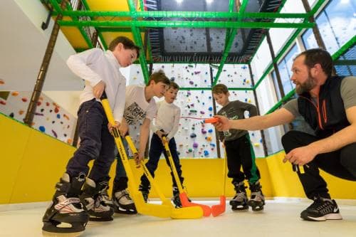 Children play indoor hockey under bright lights in a vibrant recreational center, surrounded by colorful climbing walls, creating an energetic atmosphere ideal for family-friendly activities and sports training.