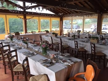 A cozy outdoor dining area under a wooden pavilion features neatly arranged tables with white linens, floral centerpieces, and rustic chairs, creating an inviting atmosphere perfect for group gatherings or events.
