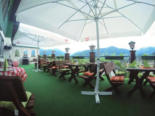 A cozy outdoor terrace with wooden tables, cushioned benches, and large umbrellas offers a serene dining spot overlooking lush mountains, ideal for travelers seeking relaxation and scenic views.