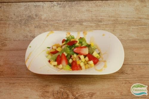 A vibrant fruit salad featuring strawberries, corn, and greens in a white bowl on a rustic wooden table, perfect for a healthy dining or food photography travel blog post.
