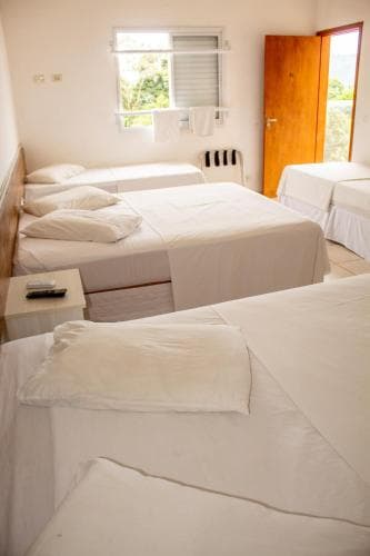 A cozy hostel room with multiple beds, white linens, natural light from windows, and a wooden door, ideal for budget travelers seeking simplicity and comfort.