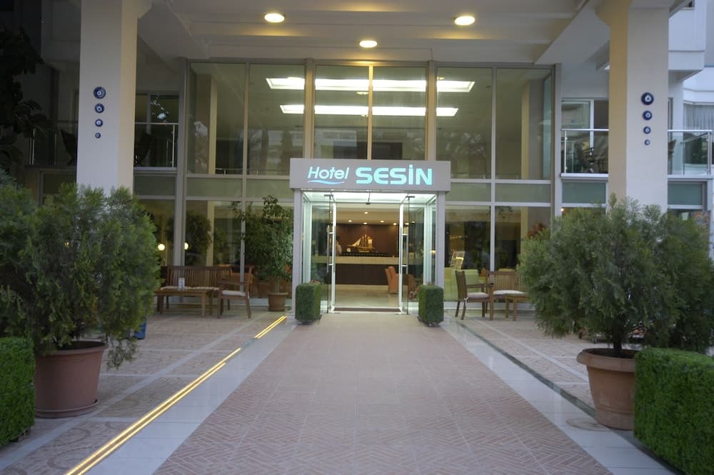 A welcoming hotel entrance with glass doors, illuminated signage, potted greenery, and a tiled pathway sets a serene and inviting mood for travelers seeking accommodation.