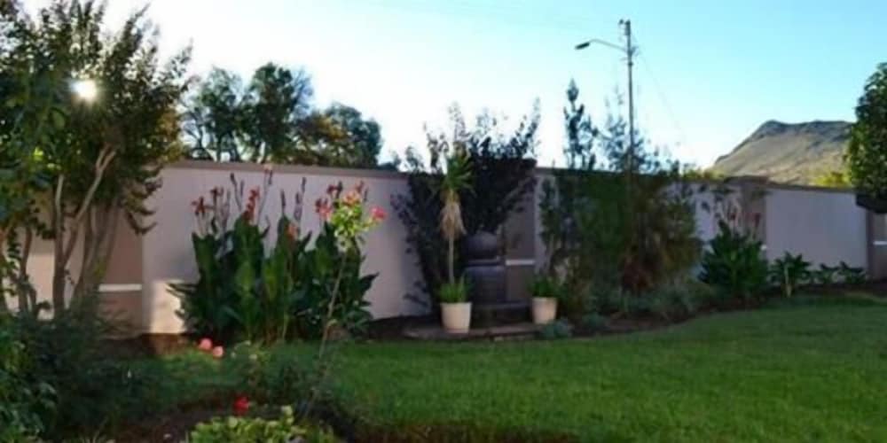 A serene suburban garden with lush greenery, vibrant flowers, and a tranquil fountain set against a backdrop of mountains, ideal for travelers seeking a peaceful retreat.