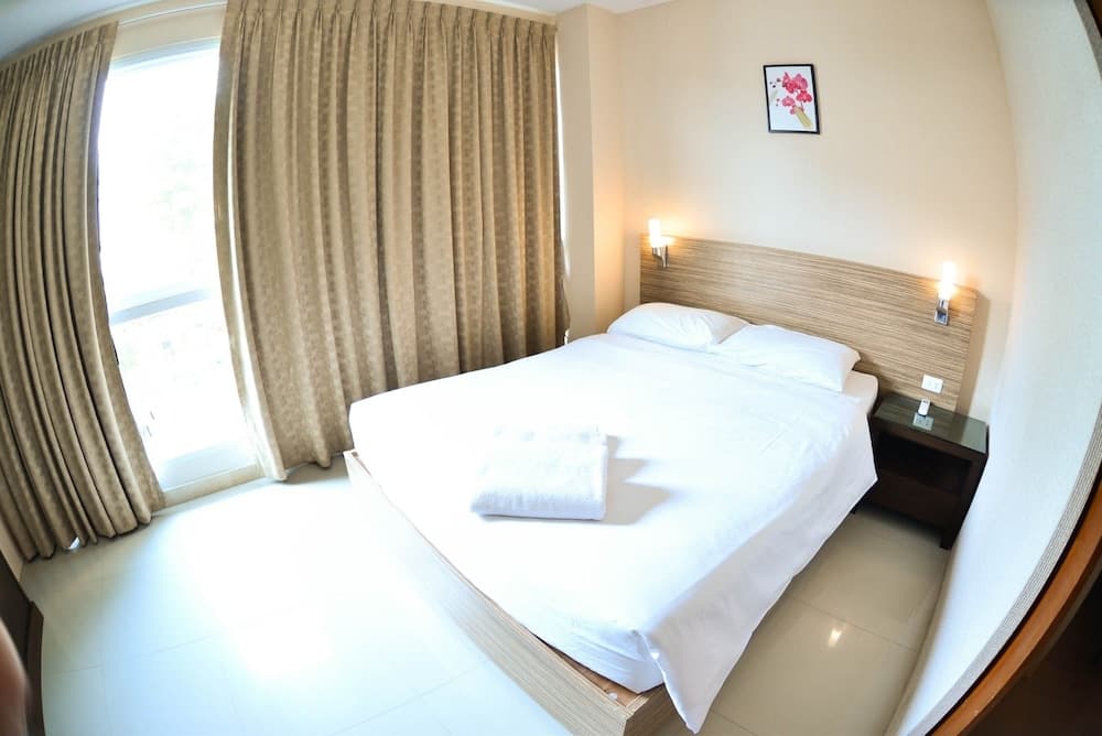 A cozy hotel room with a neatly made bed, wooden headboard, soft lighting, and large window draped with curtains, ideal for travelers seeking comfort and relaxation.