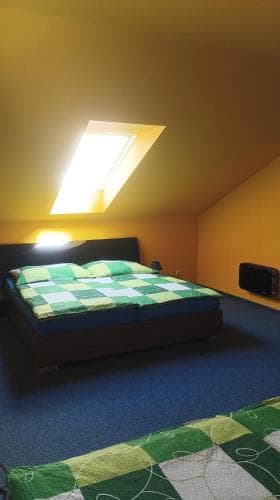 A cozy attic bedroom with slanted walls, a skylight casting warm light, and neatly arranged beds with green checkered quilts, ideal for travelers seeking a quaint and comfortable stay.